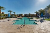 Located at 3223 N Algodon Way in Phoenix, Arizona, this expansive outdoor amenity area offers a resort-style experience designed for relaxation and recreation in the heart of the Sonoran Desert. The centerpiece of the space is a series of interconnected swimming pools with crystal-clear turquoise water, including a large lap-style pool with fountains and a separate spa, all set against a backdrop of contemporary multi-story residential buildings finished in warm stucco tones. Towering palm trees and mature shade trees are strategically placed throughout the grounds, providing natural relief from the Arizona sun. The generous stone-paved pool deck accommodates rows of lounge chairs and umbrella-shaded seating areas, offering ample space for sunbathing and socializing. A covered pergola structure provides additional shaded retreat near the water's edge. Beyond the main pool area, a thoughtfully landscaped courtyard features manicured hedges, desert-adapted shrubs, gravel accents, and patio furniture clustered beneath shade umbrellas, creating a quieter outdoor gathering space. Secure gated access to the pool equipment area ensures both safety and convenience for residents. The entire outdoor complex is bathed in abundant natural sunlight, embodying the quintessential Phoenix outdoor lifestyle.