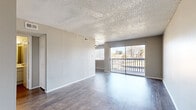 This single-floor, 1-bedroom, 1-bathroom unit offers a practical and efficient layout across a comfortable footprint. The open living room is a standout space, featuring dark wood-look laminate flooring, neutral gray walls, and a textured ceiling. A large sliding glass door floods the room with natural light and opens onto a private balcony with outdoor views of surrounding trees and greenery. Adjacent to the living room, the galley-style kitchen is equipped with white cabinetry, white countertops, a double-basin sink, and black appliances including a refrigerator and range. A ceiling fan and a dedicated window provide ventilation and additional natural light. The bedroom offers a comfortable sense of space with plush carpeting, a window with blinds, neutral gray walls, and a textured ceiling. It connects directly to a spacious walk-in closet outfitted with a full-width hanging rod and shelving. The bathroom features a full tub-shower combo with white tile surround, wood-look flooring, and a vanity with storage. A hallway connects the main living areas, completing the efficient and functional floor plan.