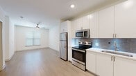 Located at 328 Cherokee Blvd in Chattanooga, Tennessee, this single-floor residence offers a clean, modern aesthetic with thoughtfully designed living spaces. The open-concept layout seamlessly connects the kitchen and living area, creating a bright and airy atmosphere enhanced by light hardwood-style flooring throughout.

The kitchen is a standout feature, equipped with a full suite of stainless steel appliances including a refrigerator, electric range, built-in microwave, and dishwasher. Crisp white cabinetry extends to the ceiling, providing generous storage, while a grey subway tile backsplash adds a stylish contrast to the white quartz-style countertops. Recessed lighting illuminates the workspace effectively.

The living area is open and spacious, bathed in natural light from windows fitted with horizontal blinds. A ceiling fan overhead adds both comfort and a functional design element. The neutral wall tones and clean lines give the space a fresh, contemporary feel.

The bathroom is well-appointed with a white vanity featuring multiple drawers, a large framed mirror, and tile flooring. An adjacent walk-in closet with built-in shelving and rod systems offers practical storage solutions.

The hallway connects all areas efficiently, with additional utility access panels and entry door visible. Overall, the unit presents a polished, move-in-ready interior suited for modern living in Chattanooga.