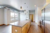 Located at 101 Virginia St in Sioux City, Iowa, this well-appointed 2-bedroom, 2-bathroom unit blends modern design with industrial character. The open-concept living, dining, and kitchen area serves as the heart of the home, anchored by a large central island with a sleek gray countertop, undermount sink, and pendant lighting. Light maple cabinetry, stainless steel appliances — including a French door refrigerator, electric range, and built-in microwave — and exposed metallic ductwork give the kitchen a contemporary, loft-inspired aesthetic. Wood-look luxury flooring flows throughout the main living areas, complementing the clean white walls and natural light streaming in through multiple windows with outdoor views. The primary bedroom offers plush carpeting, generous closet access, and its own en-suite bathroom featuring a dual-sink vanity with gray countertops, maple cabinetry, a large mirror, and a soaking tub. The second bathroom provides a similarly refined single-vanity setup with matching finishes. The second bedroom also features soft carpeting and a bright window with outdoor views. A dedicated laundry area, five closets, and a central hallway add to the unit's practical layout, making it a well-organized and functional living space.