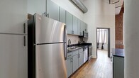 Located at 1000 Washington Ave in downtown St. Louis, this two-bedroom, two-bathroom loft showcases a compelling blend of industrial character and modern updates. Rich, reclaimed hardwood flooring runs throughout the space, complemented by soaring ceilings with exposed ductwork and a warm wood-paneled ceiling accent visible in the hallway. Structural columns and exposed brick walls add authentic loft character, while large floor-to-ceiling windows in the living area flood the space with natural light and offer urban views.

The open-concept kitchen, dining, and living area serves as the heart of the home. The kitchen is outfitted with sage-green cabinetry, dark granite countertops, stainless steel appliances, and a peninsula island — ideal for both cooking and entertaining. A central hallway connects the bedrooms, each featuring hardwood floors and clerestory-style interior windows that allow light to filter through. Bedroom doors with glass pane inserts add a refined industrial touch. Both bathrooms are appointed with granite vanities and matte black fixtures. A dedicated in-unit laundry room with full-size washer and dryer adds everyday convenience, while a utility room and ample closet space ensure practical storage throughout.