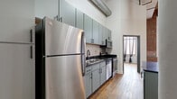 Located at 1000 Washington Ave in downtown St. Louis, this two-bedroom, two-bathroom loft showcases a compelling blend of industrial character and modern updates. Rich, reclaimed hardwood flooring runs throughout the space, complemented by soaring ceilings with exposed ductwork and a warm wood-paneled ceiling accent visible in the hallway. Structural columns and exposed brick walls add authentic loft character, while large floor-to-ceiling windows in the living area flood the space with natural light and offer urban views.

The open-concept kitchen, dining, and living area serves as the heart of the home. The kitchen is outfitted with sage-green cabinetry, dark granite countertops, stainless steel appliances, and a peninsula island — ideal for both cooking and entertaining. A central hallway connects the bedrooms, each featuring hardwood floors and clerestory-style interior windows that allow light to filter through. Bedroom doors with glass pane inserts add a refined industrial touch. Both bathrooms are appointed with granite vanities and matte black fixtures. A dedicated in-unit laundry room with full-size washer and dryer adds everyday convenience, while a utility room and ample closet space ensure practical storage throughout.