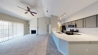This single-floor residence offers a thoughtfully designed open-concept layout that seamlessly connects the living, dining, and kitchen areas. The living room is a standout space, anchored by a white-brick fireplace with built-in shelving on either side, and crowned by dramatic vaulted ceilings that lend an expansive, airy feel. A ceiling fan keeps the space comfortable, while large vertical-blind-covered windows invite natural light throughout. Plush wall-to-wall carpeting adds warmth underfoot.

The kitchen is efficiently designed with a wraparound peninsula countertop featuring a white quartz surface and an undermount sink. Grey cabinetry lines the walls, complemented by a white tile backsplash and stainless steel appliances, including a refrigerator, range, and microwave. Track lighting overhead ensures excellent task visibility.

The bedroom is generously sized, with soft carpet, a ceiling fan, and access to a spacious walk-in closet. The bathroom features wood-look flooring, a tub-shower combo with full-height grey tile surround, and a vanity with a white countertop and grey cabinetry. The entry area transitions seamlessly between wood-look and carpeted flooring, completing this well-appointed residence.