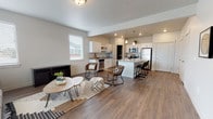 This two-story residence is designed with a clean, contemporary aesthetic throughout, combining neutral tones, wood-look flooring, and soft carpet to create a cohesive and comfortable environment. The main level opens into a bright living area, where multiple windows fitted with white blinds allow natural light to fill the space. The living room flows seamlessly into a well-equipped kitchen, creating an open-concept layout ideal for everyday living and entertaining. The kitchen features white shaker-style cabinetry, granite countertops, stainless steel appliances including a refrigerator, range, microwave, and dishwasher, and a central island with bar seating. A dedicated walk-in pantry provides generous storage. Pendant lighting above the island adds a refined touch to the space. The bathrooms are consistently finished with white cabinetry, granite countertops, large mirrors, and tub-shower combinations. The bedrooms, located on the upper level, are carpeted for comfort and each includes walk-in closet access. The overall ambiance is modern and understated, with a neutral palette and quality finishes carried consistently throughout both floors.