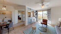 Located at 47750 Adams St in La Quinta, California, this single-floor residence offers a thoughtfully designed layout with a warm, eclectic aesthetic throughout. The open-concept living area is anchored by plush carpeting, a ceiling fan, and a sliding glass door that leads to a private balcony, allowing an abundance of natural light and outdoor views to flow into the space. Crown molding and arched architectural details add a refined touch to the interior. The kitchen features light wood cabinetry, a double-basin sink, tile flooring, and a pass-through bar with bar stool seating — ideal for casual dining. Adjacent to the kitchen, a dedicated dining area accommodates a round wooden table and is accented by bold wall art and a built-in shelving nook. The living room showcases vibrant, curated artwork and comfortable seating arranged over a patterned area rug. The bedrooms are generously sized, each with ceiling fans, carpeted floors, and ample natural light from large windows with decorative curtains. One bedroom includes a walk-in closet and a striking accent wall. The bathroom is finished with tile flooring, a shower-tub combination with sliding glass doors, and decorative wall-mounted shelving. Throughout the space, a cohesive and colorful design sensibility creates a vibrant yet comfortable living environment.