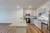 Located at 16631 E Colfax Ave in Aurora, Colorado, this thoughtfully designed 2-bedroom, 1-bathroom single-floor residence offers a clean, modern aesthetic throughout. The open-concept layout seamlessly connects the kitchen and living room, creating an efficient and welcoming common area. Rich wood-look flooring runs throughout the main living spaces, complemented by recessed lighting and a ceiling fan that enhance both function and ambiance.

The kitchen is a standout feature, boasting gray shaker-style cabinetry, granite countertops, a large center island, and a full suite of stainless steel appliances including a refrigerator, range, microwave, and dishwasher. A sliding glass door in the living area fills the space with natural light and provides outdoor access.

Both bedrooms are carpeted and bright, each featuring windows with outdoor views of surrounding greenery. The primary bedroom offers a comfortable footprint with a closet nearby. The full bathroom is finished with white cabinetry, a granite vanity, and a tub/shower combination with tile surround.

A dedicated in-unit laundry room with a full-size washer and dryer adds everyday convenience, making this a well-appointed, move-in-ready residence.