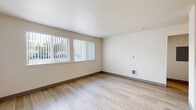 This single-floor unit offers a clean, functional layout designed for comfortable everyday living. The living area serves as the central gathering space, featuring light wood-style plank flooring, neutral beige walls, and a pair of large windows dressed with vertical blinds that allow generous natural light and outdoor views. A wall-mounted heating unit ensures year-round comfort, while ample wall space provides flexibility for furnishing arrangements.

The galley-style kitchen is efficiently designed, featuring light wood cabinetry both above and below the counter, a built-in countertop workspace, and white appliances including a refrigerator, electric range, and dishwasher. A stainless steel sink completes the setup, and the wood-style flooring carries through seamlessly from the living area.

The bedroom is a calm, private retreat with soft wall-to-wall carpeting, neutral walls, a window offering outdoor views, and a wall vent for climate control. An additional unfurnished room with matching carpet and a private door provides flexible use as a second bedroom or office.

The bathroom includes a full-size soaking tub with a curved shower rod, a single-sink vanity with light wood cabinetry and gray countertop, and neutral tile-style flooring, presenting a straightforward and tidy design throughout.