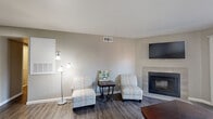 This efficiently designed single-floor residence offers a thoughtful layout encompassing a living room, dining room, kitchen, bedroom, bathroom, hallway, closet, and pantry. The living room serves as the centerpiece of the home, featuring a tiled corner fireplace, dark hardwood-style flooring, neutral gray walls, and a sliding glass door that opens to a balcony, filling the space with natural light. The kitchen is a galley-style configuration equipped with warm wood cabinetry, light stone countertops, black appliances, and direct access to a dedicated pantry with multi-tiered shelving for ample storage. Adjacent to the kitchen, the dining area provides a cozy nook with enough room for a four-seat dining set. The bedroom is a comfortable retreat with a ceiling fan, natural window light, dark hardwood-style flooring, and generous space for a full bedroom suite. The bathroom features a wood-toned vanity with a stone-style countertop, a large mirror, and a shower-tub combination. Throughout the home, consistent neutral tones, clean white trim, and dark flooring create a cohesive and modern aesthetic. Additional storage is provided by a dedicated closet and the well-shelved pantry, maximizing the practicality of the overall footprint.