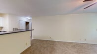 This single-floor 1-bedroom, 1-bathroom unit offers a practical and comfortable layout designed for easy everyday living. The living area is generously proportioned, finished with neutral wall-to-wall carpeting and bright, cream-toned walls that create a clean, inviting atmosphere. A ceiling fan with a light fixture provides both air circulation and ambient lighting, while multiple windows along the exterior wall allow natural light to fill the space. A sliding glass door opens directly onto a private balcony, offering pleasant outdoor views of surrounding greenery—a standout feature of the unit.

The kitchen is thoughtfully designed in an open-concept style, separated from the living space by a raised peninsula counter with a dark laminate surface, ideal for casual dining or meal prep. White cabinetry lines the kitchen walls, complemented by stainless steel appliances including a refrigerator and a range. A skylight-style ceiling fixture brightens the kitchen area effectively. Adjacent to the kitchen is a closet providing convenient storage access.

The bedroom is well-sized, carpeted, and finished consistently with the rest of the unit's neutral palette. Throughout, the unit maintains a cohesive, understated aesthetic that offers a comfortable and functional living environment.