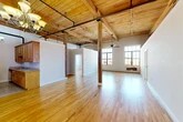 Located at 717 N Clinton St in Syracuse, NY, this two-bedroom, two-bathroom loft showcases a striking industrial aesthetic rooted in its building's historic character. The open-plan living and dining area commands attention with soaring wood-plank ceilings supported by exposed timber beams and original structural columns, creating a dramatic, loft-style atmosphere. Large multi-pane windows flood the space with abundant natural light, offering views of the surrounding neighborhood. Warm hardwood flooring extends throughout the main living areas, complementing the raw, industrial elements overhead. The galley-style kitchen is well-equipped with warm wood cabinetry, granite-style countertops, stainless steel appliances including a full-size refrigerator, and tile flooring, with an elegant chandelier adding a refined touch. Both bedrooms are finished with hardwood floors and neutral walls, providing a clean and comfortable retreat. The primary bedroom is generously sized and benefits from ample closet space, while four total closets across the unit ensure excellent storage. The bathrooms feature full tub-and-shower combinations. The unit's single-floor layout and expansive open areas make for a highly functional and visually cohesive living experience.
