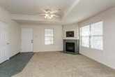 This single-story home offers a thoughtfully designed layout with a bright, open feel throughout. The living room serves as a central gathering space, featuring plush neutral carpeting, a tile-surround fireplace, and multiple windows that allow natural light to fill the room. A ceiling fan overhead adds both comfort and style. The entry door, fitted with glass panels, further enhances the sense of openness.

The kitchen is positioned adjacent to the living area in an open-concept arrangement, separated by a raised breakfast bar with a stone-look countertop. White cabinetry, including glass-front upper cabinets, pairs with white appliances and recessed lighting to create a clean, functional workspace. Dark tile flooring in this area provides a clear visual transition from the carpeted living spaces.

The bedrooms are carpeted and generously proportioned, each equipped with ceiling fans and natural light from windows with outdoor views. Select bedrooms feature tray ceilings with crown molding detailing, adding architectural interest. Closet space is well provided, with one bedroom offering both a walk-in closet and an additional built-in shelving closet.

Both bathrooms are finished with large-format gray tile flooring, tub-shower combinations with sliding glass doors, and vanities featuring stone-look countertops with undermount sinks and wood-trimmed cabinetry. The overall ambiance of the home is neutral, clean, and move-in ready.
