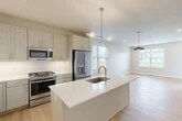 Located at 134 Kingsbury Ave in Corning, NY, this well-appointed three-story home offers a thoughtfully designed layout across three distinct levels. The main floor features an open-concept kitchen and living room bathed in natural light from multiple windows. The kitchen is a standout, showcasing a large center island with a quartz countertop and undermount sink, stainless steel appliances including a gas range, built-in microwave, and French door refrigerator, complemented by soft gray shaker-style cabinetry and a classic white subway tile backsplash. Light hardwood flooring flows throughout the main living areas, adding warmth to the clean, modern aesthetic. The upper floor hosts three bedrooms, including a generously sized primary bedroom with an en-suite bathroom featuring large-format tile flooring, a glass-enclosed shower, and a vanity with ample storage. Bedrooms are carpeted and filled with natural light. Closets include wire shelving systems for organized storage. The basement level provides additional functional space with insulated walls and a utility area housing the electrical panel. A spacious attached garage with an automatic opener and concrete flooring completes this move-in ready home.