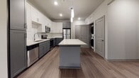 Located at 174 Overlook Point Pl in Charleston, SC 29492, this single-floor residence offers a thoughtfully designed layout with contemporary finishes throughout. The kitchen is a standout feature, showcasing a two-tone cabinetry scheme with crisp white upper cabinets and charcoal gray lower cabinets, complemented by white subway tile backsplash, light quartz countertops, and a full suite of stainless steel appliances including a refrigerator, range, over-the-range microwave, and dishwasher. A central island with pendant lighting provides additional prep space and casual seating potential. Wood-look plank flooring runs seamlessly throughout the home, adding warmth and visual continuity. Conveniently tucked near the kitchen is an in-unit laundry area with a stacked washer and dryer. The bedroom offers generous proportions, natural light through large windows with blinds, a ceiling fan, and direct access to a spacious walk-in closet with wire shelving. The bathroom is well-appointed with gray shaker-style cabinetry, a wide vanity mirror, quartz countertop, and a soaking tub with white subway tile surround. The living area is open and bright, benefiting from natural light and a ceiling fan, creating a comfortable and functional everyday living space.