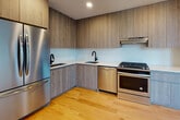 Located at 1277 E 14th St in the Flatbush neighborhood of Brooklyn, NY, this modern residence offers a thoughtfully designed single-floor layout with clean lines and contemporary finishes throughout. Warm honey-toned hardwood floors flow seamlessly across every room, lending a bright and cohesive feel to the entire space.

The living area is a standout, featuring large floor-to-ceiling windows and a glass door that opens onto a private balcony with neighborhood views, filling the room with abundant natural light. Additional bedrooms are well-proportioned, each equipped with wide windows that frame outdoor views and include built-in radiator units for heating.

The kitchen is outfitted with full-height wood-grain cabinetry, white quartz countertops, a light mosaic tile backsplash, and stainless steel appliances including a gas range, dishwasher, and French door refrigerator. Matte black fixtures add a modern contrast throughout.

Two bathrooms serve the residence. The primary bath features a frameless sliding glass walk-in shower with large-format wall tiles and penny tile flooring, paired with a wood-tone vanity and white countertop. The secondary bathroom offers a soaking tub with shower, matching vanity, and coordinating tile finishes. The space also includes a utility panel and ample closet storage.