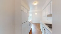 This single-floor unit offers a practical and well-organized layout designed for comfortable everyday living. The galley-style kitchen is efficiently arranged with white cabinetry featuring gold-toned hardware, a white appliance suite including a refrigerator and electric range, a built-in sink, and laminate wood flooring that runs underfoot. Upper and lower cabinets provide ample storage, and the kitchen opens toward a dining area accented by an elegant chandelier pendant light, adding a touch of warmth to the space.

The living and dining areas transition smoothly, with rich hardwood-style flooring throughout and large windows dressed in vertical blinds that invite generous natural light and views of the surrounding greenery. The open layout creates a connected, airy feel between the main living spaces.

The bedrooms are carpeted for comfort, each offering neutral walls, natural light from well-positioned windows, and closet storage. One bedroom features a louvered bifold closet door, while another benefits from an expansive sliding glass door that frames outdoor views.

The bathroom is clean and functional, outfitted with a single-sink vanity topped with a light countertop, a mirrored medicine cabinet, and a full tub-shower combination with white tile surround. Consistent hardwood-style flooring ties the bathroom to the rest of the unit's cohesive design.