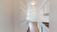 This single-floor unit offers a practical and well-organized layout designed for comfortable everyday living. The galley-style kitchen is efficiently arranged with white cabinetry featuring gold-toned hardware, a white appliance suite including a refrigerator and electric range, a built-in sink, and laminate wood flooring that runs underfoot. Upper and lower cabinets provide ample storage, and the kitchen opens toward a dining area accented by an elegant chandelier pendant light, adding a touch of warmth to the space.

The living and dining areas transition smoothly, with rich hardwood-style flooring throughout and large windows dressed in vertical blinds that invite generous natural light and views of the surrounding greenery. The open layout creates a connected, airy feel between the main living spaces.

The bedrooms are carpeted for comfort, each offering neutral walls, natural light from well-positioned windows, and closet storage. One bedroom features a louvered bifold closet door, while another benefits from an expansive sliding glass door that frames outdoor views.

The bathroom is clean and functional, outfitted with a single-sink vanity topped with a light countertop, a mirrored medicine cabinet, and a full tub-shower combination with white tile surround. Consistent hardwood-style flooring ties the bathroom to the rest of the unit's cohesive design.