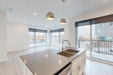 Located at 3001 Leavenworth Street in Omaha, Nebraska, this modern 2-bedroom, 2-bathroom residence offers a thoughtfully designed single-floor layout with clean, contemporary finishes throughout. The open-concept kitchen and living area serves as the heart of the home, anchored by a large center island with quartz countertops, a double undermount sink, and sleek pendant lighting. White shaker cabinetry, a tile backsplash, and stainless steel appliances complete the kitchen. Floor-to-ceiling windows flood the living area with natural light and provide sweeping views of the surrounding neighborhood, while a balcony extends the living space outdoors. Light wood-look flooring runs throughout the main areas, adding warmth to the bright, neutral palette. The primary bedroom features plush carpeting, a ceiling fan, and access to two closets, including a walk-in closet with built-in wire shelving. The primary bathroom is appointed with a dual-sink vanity, dark quartz countertops, white cabinetry, and a large mirror with overhead lighting. The second bedroom is generously sized with carpeting and easy hallway access. A connecting hallway ties together all rooms efficiently, and two closets provide ample storage throughout the residence.