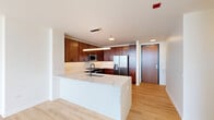 Located in Chicago's vibrant West Loop neighborhood, this well-appointed 2-bedroom, 2-bathroom residence offers a thoughtfully designed open-concept layout with modern finishes throughout. Light hardwood flooring flows seamlessly across the entire living space, complementing the clean, contemporary aesthetic.

The kitchen is a standout feature, boasting rich dark-wood cabinetry that extends to the ceiling, a large quartz waterfall island with an undermount sink, stainless steel appliances including a gas range, built-in microwave, and French door refrigerator, all illuminated by a sleek pendant light fixture. The kitchen opens directly into the combined dining and living area, which is bathed in natural light from dramatic floor-to-ceiling windows offering expansive, elevated views of the Chicago skyline and surrounding cityscape.

The generously sized primary bedroom features its own wall of floor-to-ceiling windows and a ceiling fan, alongside a walk-in closet with built-in wire shelving. The second bedroom is equally bright and well-proportioned. Both bathrooms are finished with light wood vanities, white quartz countertops, large illuminated mirrors, black hardware accents, and neutral tile flooring. Three closets throughout the residence provide ample storage for everyday living.