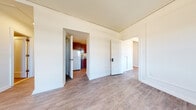Located at 205 Scott St in Wausau, Wisconsin, this single-floor unit offers a straightforward, functional layout with a clean, neutral aesthetic throughout. The main living areas feature updated light-toned luxury vinyl plank flooring that extends consistently across the space, complementing the bright white walls and creating a cohesive, well-maintained feel.

The open main area connects to multiple rooms via white-paneled doors, allowing for flexible use of space. One room features a ceiling fan with a light fixture and decorative wall paneling, while another benefits from a double-hung window offering views of the Wausau cityscape and surrounding area. Baseboard heating units run along the exterior walls, ensuring efficient climate control throughout.

The kitchen is compact and efficiently designed, featuring rich dark-stained wood cabinetry, a stainless steel sink, grey laminate countertops, and a white electric range with a ventilation hood above. A full-size white refrigerator completes the appliance package.

The bathroom includes a full bathtub and shower combination with chrome fixtures, a toilet, and classic white tile flooring, maintaining the clean, functional character found throughout the rest of the space.
