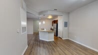 This single-story residence offers a well-designed, open-concept layout that seamlessly connects the main living and kitchen areas. Rich hardwood-style flooring flows throughout the living spaces, creating a warm and cohesive aesthetic. The kitchen is a functional centerpiece, featuring dark wood cabinetry, granite countertops, and a full suite of stainless steel appliances, including a refrigerator, range, and over-the-range microwave. A peninsula with a granite surface and built-in sink extends into the dining area, illuminated by pendant lighting suspended from above. The open living area is generously proportioned, with neutral-toned walls, a ceiling fan with light fixture, and sliding glass doors that allow natural light to pour in while providing outdoor access. A dedicated laundry room houses a full-size washer and dryer with built-in shelving above. Two bathrooms serve the residence: one features a walk-in glass-door shower, dark wood vanity, and wood-look tile flooring, while the second includes a tub-shower combination and a dual-sink vanity. A utility panel is conveniently accessible near the kitchen. The overall ambiance is clean, modern, and move-in ready.