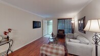 Located at 10522 Beechnut St in Houston, Texas, this single-story home offers a well-organized and comfortable layout throughout. The living room serves as the heart of the home, featuring rich hardwood flooring, crown molding, and large windows dressed with floor-length drapes that allow natural light to filter in. A wall-mounted television and access to an exterior door make the space both functional and welcoming.

The galley-style kitchen is efficiently designed with ample white cabinetry, granite-look countertops, a double sink, and white appliances including a range and refrigerator. Light tile flooring keeps the space bright and easy to maintain. Adjacent to the kitchen, a dedicated dining area accommodates intimate gatherings beneath an elegant chandelier, finished with the same crown molding detail found throughout the home.

The bedrooms continue the warm hardwood flooring and crown molding aesthetic. The primary bedroom features a ceiling fan, natural light from a window with sheer curtains, and generous floor space. A secondary bedroom offers a cozy, charming atmosphere with its own window and decorative touches.

The bathroom includes tile flooring, a tub-shower combination, and a clean, functional layout. Overall, this home presents a consistent, well-maintained interior with classic detailing throughout.