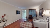 Located at 10522 Beechnut St in Houston, Texas, this single-story home offers a well-organized and comfortable layout throughout. The living room serves as the heart of the home, featuring rich hardwood flooring, crown molding, and large windows dressed with floor-length drapes that allow natural light to filter in. A wall-mounted television and access to an exterior door make the space both functional and welcoming.

The galley-style kitchen is efficiently designed with ample white cabinetry, granite-look countertops, a double sink, and white appliances including a range and refrigerator. Light tile flooring keeps the space bright and easy to maintain. Adjacent to the kitchen, a dedicated dining area accommodates intimate gatherings beneath an elegant chandelier, finished with the same crown molding detail found throughout the home.

The bedrooms continue the warm hardwood flooring and crown molding aesthetic. The primary bedroom features a ceiling fan, natural light from a window with sheer curtains, and generous floor space. A secondary bedroom offers a cozy, charming atmosphere with its own window and decorative touches.

The bathroom includes tile flooring, a tub-shower combination, and a clean, functional layout. Overall, this home presents a consistent, well-maintained interior with classic detailing throughout.