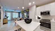 Located at 8072 Poinciana Blvd in Orlando, Florida, this single-story residence offers a well-designed, contemporary living experience. The open-concept layout connects the kitchen and living area seamlessly, creating an inviting and functional space. The kitchen is a standout feature, outfitted with crisp white shaker cabinetry, stainless steel appliances including a range, microwave, dishwasher, and refrigerator, complemented by white quartz countertops and a large central island with pendant lighting overhead. Light wood-look tile flooring runs throughout, enhancing the bright, airy feel. The living area is characterized by a bold textured accent wall, a ceiling fan, and a generous window that draws in natural light. The bedroom is a calm retreat, featuring soft blue-toned walls, a ceiling fan, and a large window with sheer draping. Two bathrooms serve the residence — one featuring a glass-enclosed walk-in shower, white vanity cabinetry, and pendant lighting, while the second offers a clean, minimalist design with open shelving. A dedicated in-unit laundry area houses a full-sized top-loading washer and dryer with overhead shelving. Throughout the home, recessed lighting, neutral tones, and modern finishes create a cohesive and polished aesthetic.