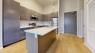 This well-appointed 2-bedroom, 2-bathroom residence is thoughtfully designed across a single floor, combining modern aesthetics with functional living. The open-concept kitchen serves as the heart of the home, featuring sleek gray flat-front cabinetry extending to the ceiling for ample storage, white quartz countertops, and a full suite of stainless steel appliances including a range, built-in microwave, and refrigerator. A central kitchen island with an integrated sink and pendant lighting above adds both style and convenience, making it ideal for cooking and casual dining. Light wood-tone flooring runs throughout the kitchen and main living areas, lending warmth and continuity to the space. Both bedrooms are carpeted and generously proportioned, each featuring neutral-toned walls and windows fitted with horizontal blinds that allow for natural light. The two bathrooms are finished consistently, with dark wood vanities, white countertops, and light wood-look flooring that complement the overall design palette. In-unit laundry is also present, adding everyday convenience. The residence presents a clean, contemporary feel throughout, with a cohesive material palette and a layout that makes efficient use of every square foot.