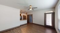 This single-story, one-bedroom, one-bathroom residence in Houston, TX offers a thoughtfully designed open-concept layout finished with warm wood-style flooring that flows consistently throughout the space. The living area is anchored by a ceiling fan with integrated lighting, creating a comfortable and functional gathering space. A peninsula-style kitchen seamlessly connects to the living area, featuring granite countertops with an undermount sink, light wood cabinetry, stainless steel appliances including a French door refrigerator, microwave, and electric range, and pendant lighting overhead for an inviting ambiance. The bedroom is a well-proportioned retreat with its own ceiling fan, a window fitted with blinds for natural light and privacy, and the same durable wood-style flooring. The bathroom maintains the unit's modern aesthetic with dark-toned cabinetry, a granite-topped vanity, a framed mirror, and overhead vanity lighting. Dark-trimmed interior doors and bold baseboards provide a cohesive contrast against the neutral white walls, lending the space a clean, contemporary feel throughout.
