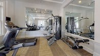 Located at 100 Preston Woods Trail in Sandy Springs, Georgia, this fitness center offers a well-equipped, single-floor workout space designed to support a comprehensive exercise routine. The room is bathed in abundant natural light streaming through multiple large windows that frame views of the surrounding mature trees, creating an energizing and welcoming atmosphere.

The interior features a neutral color palette of crisp whites and soft grays, complemented by a tray ceiling with crown molding, recessed lighting, and a ceiling fan that enhances air circulation throughout the space. Floor-to-ceiling mirrors line portions of the walls, amplifying the sense of openness while allowing for proper form checks during workouts.

The fitness center is outfitted with professional-grade Cybex cardio equipment, including treadmills, an elliptical trainer, and a recumbent cycle. A dedicated strength training area houses a Cybex functional trainer cable machine along with a multi-station weight machine, providing a full range of resistance training options. A dumbbell rack with a full set of free weights and a flat weight bench round out the strength section, while a stability ball adds versatility for core work. The flooring consists of a durable, patterned carpet tile that offers comfort and traction throughout. Together, these elements create a polished, fully functional fitness facility suited for a wide range of workout needs.