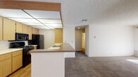 Located at 38441 Fifth St W in Palmdale, California, this single-floor residence offers a practical and comfortable layout with several notable features throughout. The living room serves as the heart of the home, showcasing a wood-paneled fireplace surround flanked by built-in shelving, adding warmth and character to the space. Vertical blinds line a large window, allowing natural light to filter across the plush carpeted flooring. The kitchen is thoughtfully designed with light oak cabinetry, a paneled grid ceiling light fixture, and a peninsula with a laminate countertop that doubles as a breakfast bar. Black appliances, including a refrigerator, gas range, and over-the-range microwave, complete the functional cooking space, while hardwood-style flooring adds a clean finish underfoot. The bedrooms are generously proportioned, each featuring soft carpeting and windows with vertical blinds that invite natural light. Two bathrooms mirror each other in design, each outfitted with oak vanity cabinetry, speckled countertops, large mirrors, and hardwood-style flooring. One bathroom includes a shower/tub combination. A textured ceiling is consistent throughout the home, contributing to its cohesive interior aesthetic.