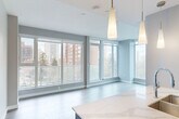 Located in Edmonton's vibrant Oliver neighbourhood, this modern 2-bedroom, 1-bathroom unit offers a thoughtfully designed open-concept layout finished with light hardwood flooring throughout. The combined kitchen and living area is a standout feature, bathed in natural light streaming through expansive floor-to-ceiling windows that frame urban views of the surrounding cityscape. A sliding glass door leads to a private balcony, further enhancing the bright and airy atmosphere.

The kitchen is well-appointed with two-tone cabinetry — white uppers paired with dark wood lower cabinets — complemented by a white quartz countertop, subway tile backsplash, stainless steel appliances including a full-size refrigerator and range, and elegant pendant lighting above the island peninsula.

Both bedrooms are generously proportioned, each benefiting from large windows with city views and light hardwood flooring. The primary bedroom includes a built-in closet, while the second bedroom also features closet storage. The bathroom is finished with marble-style wall surrounds encasing a full soaker tub and tub surround, paired with clean white fixtures. The unit is completed by a dedicated entrance, offering a practical and welcoming arrival experience.