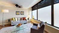 This single-floor residence offers two bedrooms and two bathrooms within a thoughtfully designed layout that balances comfort and modern style. The living room is a standout space, featuring expansive floor-to-ceiling windows fitted with roller shades that bathe the room in natural light while offering privacy. A ceiling fan, hardwood-style flooring, and a glass coffee table contribute to the room's contemporary, airy feel.

The dining area makes a strong visual impression with a bold amber accent wall, hardwood-style flooring, and a classic chandelier overhead. A glass-top dining table with dark leather chairs anchors the space, complemented by coordinating wall art.

The kitchen is outfitted with rich dark cabinetry, dark countertops, a white tile backsplash, and a full suite of stainless steel appliances including a range, microwave, dishwasher, and refrigerator. Recessed lighting enhances functionality.

Both bedrooms feature soft carpet, neutral tones, double closets, and warm ambient lighting. The primary bedroom includes ample closet storage with double doors.

The two bathrooms are finished with light tile flooring and shower-tub combinations, maintaining a clean and practical aesthetic throughout.