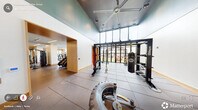 Located at 1001 Hammell Dr in Raleigh, NC, this professional-grade fitness center delivers a comprehensive workout experience across a generously sized single-floor layout. The space is thoughtfully divided into distinct functional zones, each designed to support a variety of training disciplines.

The cardio area features a row of treadmills and stationary bikes positioned near large windows, flooding the space with natural light and providing outdoor views that make workouts more enjoyable. Adjacent to this zone, a dedicated strength training area is outfitted with a full rack of dumbbells, adjustable benches, cable machines, and Hammer Strength equipment, all reflected in floor-to-ceiling mirrors that enhance the sense of openness.

A separate functional training zone stands out with soaring ceilings, a teal accent ceiling, and an Octagon multi-functional rig complete with TRX suspension trainers, a heavy punching bag, and battle ropes. This high-bay area is bathed in natural light from an expansive clerestory window wall. Durable rubber flooring throughout ensures safety and comfort across all workout areas.

The overall design balances a clean, modern aesthetic—featuring white walls, warm wood accents, and recessed linear lighting—with a practical, high-performance layout suited for a wide range of fitness routines.