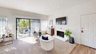 Located at 1142 Buckingham Dr in Costa Mesa, California, this well-appointed one-bedroom, two-bathroom home offers a thoughtfully designed single-floor layout filled with natural light. The open-concept living, dining, and kitchen area forms the heart of the home. The bright living room features plush carpeting, large sliding glass doors leading to a private balcony with outdoor views, and a clean white-paneled fireplace as a focal point. The dining area is anchored by a modern chandelier and a generous window that frames greenery outside. The kitchen is efficiently laid out with white cabinetry, stainless steel appliances including a gas range and refrigerator, wood-look flooring, and a tray ceiling detail. The spacious primary bedroom offers soft carpet, natural light through vertical blinds, and access to three closets, including a large walk-in. The primary bathroom features a dual-sink vanity with stone-toned countertops and white cabinetry, while the second bathroom includes a tub/shower combination. A versatile den provides additional flexible living space. Completing the home are a dedicated laundry area and a hallway connecting all rooms seamlessly.