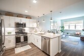 Located at 2930 Rockaway Ave in Oceanside, NY, this one-bedroom, one-bathroom residence offers a thoughtfully designed single-floor layout with modern finishes and a bright, welcoming ambiance. The open-concept kitchen is a standout feature, outfitted with crisp white shaker cabinetry, a white subway tile backsplash, stainless steel appliances including a gas range, microwave, and dishwasher, and a peninsula with a double-basin sink and quartz-style countertops. Stylish pendant lighting in a brushed brass finish adds warmth to the space. The kitchen flows seamlessly into the living area, which is bathed in natural light from large windows overlooking the surrounding neighborhood. Soft blue-gray walls and warm wood-tone flooring carry throughout, creating a cohesive and calming aesthetic. The bedroom is generously proportioned, featuring two closets—including a walk-in—and a bright window that enhances the airy feel. The bathroom is finished with white subway tile, a white vanity with a gray countertop, and chrome fixtures, offering a clean and polished look. Overall, this residence combines functional design with contemporary style in a well-lit, comfortable living environment.