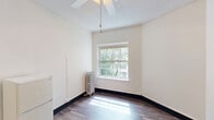 Located at 1410 SW Broadway in the heart of Portland, Oregon, this one-bedroom, one-bathroom unit offers a practical and functional layout across a single floor. The main living area features dark hardwood-style flooring and crisp white walls, creating a clean, neutral backdrop. A ceiling fan is centrally mounted beneath a textured ceiling, and a large single-pane window allows natural light to fill the room while offering views of the surrounding greenery. A classic cast-iron radiator provides supplemental heating.

The kitchen is efficiently designed with warm wood cabinetry, a stainless steel sink with dark countertops, a white electric range, and a full-size refrigerator — providing all the essentials within a compact footprint. Crown molding adds a subtle architectural detail throughout the space.

The bedroom is a generously proportioned room featuring the same hardwood-style flooring, a wide window that draws in natural light, another cast-iron radiator, and a ceiling fan, making it a comfortable and well-ventilated retreat.

The bathroom is finished with classic white subway tile in the shower area, maintaining a clean and timeless aesthetic. Overall, this unit offers a straightforward, functional living space in a prime Portland location.