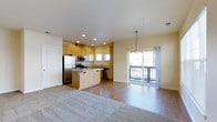 This two-floor residence offers a thoughtfully designed open-concept layout that seamlessly connects the kitchen and living areas, creating a bright and functional space. The kitchen is well-appointed with warm honey-toned wood cabinetry, stainless steel appliances including a refrigerator, microwave, and gas range, and a central island that serves as both a prep space and a casual gathering spot. A tile backsplash and ample cabinetry provide both style and storage, while recessed lighting illuminates the space efficiently. The kitchen flows naturally into the living area, where light wood-style flooring transitions into plush carpeting, adding warmth and comfort underfoot. A pendant chandelier anchors the dining or living zone, complementing the recessed lighting throughout. Large sliding glass doors flood the main living area with natural light and open directly onto a private balcony, offering pleasant outdoor views and excellent indoor-outdoor connectivity. The neutral, light-toned walls and clean finishes throughout lend the space a fresh, move-in-ready feel. With two floors, this residence provides a versatile layout suited for a variety of living arrangements, offering both shared common areas and private retreats across its levels.