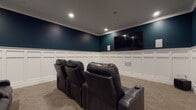 Located at 38401 Mentor Ave in Willoughby, Ohio, this single-floor space is purpose-built as a private home theater, designed to deliver an immersive cinematic experience. The room immediately commands attention with its bold deep teal upper walls, which contrast strikingly against the crisp white board-and-batten wainscoting that lines the lower half of every wall. Elegant crown molding ties the two elements together, lending the space a polished, refined character. Recessed ceiling lighting provides carefully controlled illumination, enhancing the theater ambiance while keeping the focus on the large wall-mounted flat-screen display positioned at the front of the room. Rows of black leather recliner seats with integrated cup holders are arranged to face the screen, offering a comfortable and well-organized viewing arrangement suitable for multiple guests. The neutral-toned carpet underfoot adds warmth and helps with acoustics, contributing to the room's overall cinematic feel. Framed artwork adorns the rear teal wall, adding a decorative touch that elevates the space beyond a purely functional setup. The layout is thoughtfully designed, with clearly defined viewing zones and ample room to move between seating rows. This space serves as a standout entertainment retreat, combining sophisticated architectural details with practical home theater functionality.