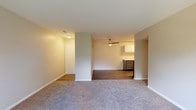 This single-floor residence offers a practical and well-organized layout that flows naturally from the living areas through to the private spaces. The main living and dining area is spacious and open, finished with neutral-toned carpet and warmed by soft ambient lighting. A ceiling fan overhead adds functionality, while a partial dividing wall subtly separates the living zone from the adjoining kitchen area.

The galley-style kitchen is efficiently designed, featuring two-tone cabinetry with white upper cabinets and grey lower cabinets, white countertops, a stainless steel sink, and black appliances including a gas range and dishwasher. Wood-look flooring runs throughout the kitchen, adding a clean contrast to the surrounding carpeted areas. A louvered closet door near the kitchen provides additional storage access.

The bedrooms are carpeted and generously sized, each benefiting from large windows that invite natural light and offer views of lush, tree-lined outdoor surroundings. The neutral wall tones throughout create a calm, cohesive atmosphere.

The bathroom is cleanly appointed with wood-look flooring, a grey vanity with a white countertop and single sink, a full tub and shower combination with white tile surround, and brushed nickel fixtures and hardware throughout.