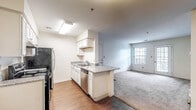 This single-floor residence is designed with a practical, open layout that connects the kitchen and living areas seamlessly. The kitchen is well-appointed with white cabinetry extending to the upper walls, granite-look countertops, stainless steel appliances including a refrigerator, electric range, and dishwasher, and hardwood-style flooring. A peninsula counter defines the boundary between the kitchen and the adjoining living space, which transitions to plush carpeting. The living area is generously sized, receiving natural light from a large window and a glass patio door that opens to an outdoor area.

The bedrooms are carpeted and bright, each featuring windows that bring in natural light and views of greenery. One bedroom includes access to a spacious walk-in closet outfitted with wire shelving along multiple walls, offering substantial storage capacity.

The unit includes two full bathrooms, each featuring white cabinetry with granite-look countertops, a tub-shower combination, and hardwood-style flooring. The overall color palette is neutral throughout, with white walls and trim contributing to a clean, cohesive aesthetic across the entire space.