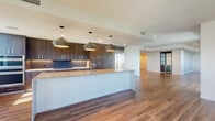 Located along South Dixie Highway in the heart of Coral Gables, Florida, this single-floor residence showcases a clean, contemporary design with high-quality finishes throughout. Warm wood-tone flooring flows seamlessly across the entire unit, anchoring a cohesive and modern aesthetic.

The open-concept kitchen serves as the centerpiece of the living space, featuring a generous granite-topped island with an undermount sink, dark wood cabinetry extending floor to ceiling, a dark tile backsplash, and stainless steel double wall ovens. Three statement pendant lights hang above the island, adding visual depth and task lighting. A stainless steel refrigerator anchors the cabinetry wall, while large windows invite abundant natural light into the space.

The living areas are bright and airy, with recessed lighting, ceiling fans, and multiple windows offering views of the surrounding Coral Gables landscape. The bedrooms are well-proportioned with clean white walls and ample natural light.

Bathrooms are finished with granite countertops, dark wood vanities, LED-backlit mirrors, glass-enclosed showers, and large-format tile flooring, offering a spa-like atmosphere. A hallway laundry closet with a stacked washer and dryer adds everyday convenience. The overall layout is thoughtfully designed to maximize flow and functionality throughout.