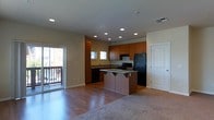 This two-floor residence offers a well-designed open-concept layout that seamlessly connects the living and kitchen areas. The main living space features a combination of hardwood flooring and plush carpeting, creating distinct zones for relaxing and entertaining. Recessed lighting throughout ensures the space is well-lit and inviting.

The kitchen is a standout feature, equipped with rich warm-toned wood cabinetry that extends to the ceiling for ample storage. A central island with a granite countertop provides additional workspace and serves as a natural gathering point. Black appliances, including a refrigerator and range, complement the cabinetry, while a sink beneath a window allows for natural light during meal preparation.

Sliding glass doors lead out to a private balcony, offering outdoor space and natural light that brightens the interior. The open sightlines between the kitchen and living area enhance the sense of spaciousness throughout the main floor.

The two-floor layout provides clear separation between living and private spaces, adding a sense of depth and versatility to the home. Overall, the space combines functional design with warm, contemporary finishes to create a comfortable and practical living environment.