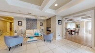 Located at 5 Promenade Blvd in Fair Lawn, NJ, this single-floor communal space is thoughtfully designed to offer both comfort and sophistication. The grand lobby welcomes visitors with gleaming large-format tile flooring, coffered ceilings with recessed lighting, and a mosaic tile accent wall flanking a sleek linear fireplace. A seating area with contemporary furnishings — including a white leather sofa, glass coffee table, and accent chairs — creates an inviting atmosphere just inside the entrance.

Wide corridors connect the various areas of the space, maintaining a clean and polished aesthetic with tray ceilings and wall sconce lighting throughout. The formal dining room is a standout feature, appointed with white wainscoting, textured wallcovering, a tray ceiling with crown molding, hardwood flooring, and natural light filtering through sheer-draped windows. A large conference-style dining table with ornate wood chairs anchors the room, complemented by a wall-mounted display screen for functional versatility.

An expansive open gathering area offers additional seating arrangements and dining options, featuring the same striking coffered ceiling design and light hardwood floors. Multiple windows provide natural light, enhancing the warm, neutral tones throughout. This well-appointed space is ideal for community gatherings, meetings, and social events.