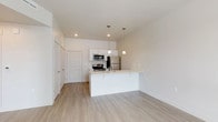 This single-floor residence offers a clean, contemporary design with a neutral color palette and thoughtful layout throughout. The open-concept living and kitchen area serves as the heart of the unit, where light hardwood-style flooring flows seamlessly underfoot. The kitchen is outfitted with white cabinetry, a stainless steel appliance suite including a refrigerator, electric range, and over-the-range microwave, and a light-toned countertop peninsula. Stylish pendant lights hang above the peninsula, adding a refined touch to the space. The adjacent living area is bright and airy, benefiting from a large window that fills the room with natural light and offers views of the surrounding cityscape.

The bedroom continues the light, understated aesthetic with soft carpeting, neutral walls, and a sizable window fitted with horizontal blinds that frame outdoor views. The space is quiet and well-proportioned, offering a comfortable retreat.

The bathroom is designed for both functionality and comfort, featuring a wide vanity with white cabinetry, ample drawer and cabinet storage, a large mirror with overhead lighting, and open shelving for additional organization. The overall ambiance of the unit is modern and move-in ready, with consistent finishes that create a cohesive and welcoming living environment.