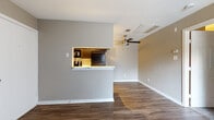 This single-floor unit offers a well-organized layout designed for comfortable everyday living. The open living area is finished with rich, dark hardwood-style flooring and neutral gray walls, creating a clean and modern aesthetic. A ceiling fan overhead adds both style and function to the space. The kitchen is efficiently arranged in a galley configuration, featuring dark cabinetry, marble-look countertops, a stainless steel sink, track lighting, and black appliances including a refrigerator and range. A pass-through window with a marble-look ledge connects the kitchen to the living area, enhancing the sense of openness and allowing for easy interaction between spaces. The bedroom provides a comfortable retreat with plush carpeting, warm neutral-toned walls, and a window dressed with blinds that allows natural light to filter in. The bathroom is neatly appointed with dark cabinetry, a marble-look countertop vanity, a large mirror, brushed nickel fixtures, and wood-style flooring that ties the space together cohesively. Throughout the unit, consistent finishes and thoughtful details contribute to a cohesive and functional living environment.