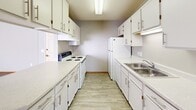 This single-floor, one-bedroom, one-bathroom unit is thoughtfully laid out to maximize its compact footprint. The open living area is the heart of the space, featuring neutral-toned carpet flooring, a textured ceiling, and a large picture window that draws in generous natural light, creating a bright and inviting atmosphere. Warm wood baseboards provide a subtle contrast against the light walls throughout.

The galley-style kitchen runs parallel along both walls, offering ample white cabinetry for storage, white appliances including a range, refrigerator, and dishwasher, and a double stainless steel sink. Light wood-look flooring adds a clean, practical touch. A pass-through counter connects the kitchen to the living area, enhancing the sense of openness.

The bedroom is a comfortable size, outfitted with plush carpet, a window with blinds, and notably features two separate closets with bifold doors and built-in hanging rods, providing excellent storage capacity.

The bathroom includes light wood-look flooring, a single-sink vanity with white cabinetry, a full tub-shower combo, and a wall-mounted mirror with overhead lighting, maintaining the clean, neutral aesthetic found throughout the rest of the unit.
