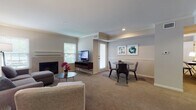 This single-floor residence offers a thoughtfully designed layout with distinct living, dining, sleeping, and utility areas. The living room serves as the central gathering space, featuring a tile-surround fireplace, crown molding, recessed lighting, and neutral carpet flooring. Natural light enters through multiple windows fitted with blinds, and a glass door provides additional brightness. Abstract framed artwork adds decorative character to the walls throughout the space.

The dining area is positioned adjacent to the living room, accommodating a round glass-top table with upholstered chairs, creating a functional yet stylish setting. The kitchen is equipped with rich cherry-toned cabinetry, dark granite countertops, stainless steel appliances including a refrigerator and dishwasher, a double sink, and light tile flooring.

The bedroom is generously proportioned, offering carpet flooring, multiple windows with outdoor views, and ample space for a king-sized bed and additional furnishings. A dedicated workspace area and closet access add practicality to the room.

The bathroom features full tile surround walls, a bathtub with a glass sliding door enclosure, and coordinating tile flooring. A dedicated in-unit laundry area with a full-sized washer and dryer rounds out this well-equipped residence.