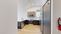 This thoughtfully designed one-bedroom, one-bathroom residence at 188 Broadway in Woodcliff Lake, NJ offers a clean, modern aesthetic across a well-proportioned single-floor layout. Light hardwood flooring runs throughout, complementing the bright white walls and dark accent baseboards that define the contemporary style.

The open-concept kitchen and living area serves as the heart of the home. The kitchen is outfitted with two-toned cabinetry — dark lower cabinets paired with warm wood-grain upper cabinets — white quartz countertops, a peninsula with a sink, and a full suite of stainless steel appliances including a refrigerator with ice maker, range, microwave, and dishwasher. Recessed lighting and a large window bring in natural light, making the space feel bright and functional.

The living area flows naturally from the kitchen and features large windows with roller shades that frame outdoor views of the surrounding greenery. The bedroom is a comfortable, well-lit room with multiple windows, an individual climate control unit, and access to two closets.

The bathroom is finished to a high standard, featuring a wood-grain vanity with a white countertop, matte black fixtures, an illuminated mirror, large-format floor tiles, and a sliding glass-enclosed tub and shower. A dedicated laundry area rounds out the functional offerings of this well-appointed residence.