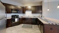 This thoughtfully laid-out one-bedroom, one-bathroom residence offers a cohesive blend of modern finishes and functional design across a single floor. The open-concept kitchen and living area serves as the heart of the home, anchored by a curved breakfast bar peninsula with pendant lighting above. The kitchen is well-appointed with rich dark-stained cabinetry, light countertops, a white subway tile backsplash, stainless steel refrigerator, and black appliances, all set on durable wood-look flooring. The living area flows naturally from the kitchen, bathed in natural light from a large window, and features a ceiling fan overhead. Neutral gray tones throughout create a calm, cohesive ambiance. The bedroom is a comfortable and private retreat, featuring plush carpet, a large window with outdoor views, and access to a balcony, filling the room with natural light. The full bathroom includes a tiled tub-shower combination, tile flooring, and a dark vanity, maintaining the consistent design aesthetic of the home. Additional spaces include a closet and a utility room, adding practical storage and functionality. The overall layout is efficient and well-connected, offering a comfortable living experience.